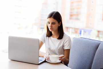 Beautiful happy woman working on laptop computer during coffee break in cafe bar