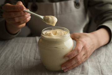 Glass jar of mayonnaise and a white spoon in hand.