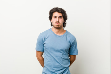 Young handsome man against a white background blows cheeks, has tired expression. Facial expression concept.