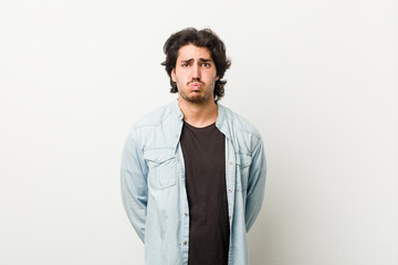 Young handsome man against a white background blows cheeks, has tired expression. Facial expression concept.