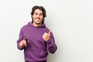 Young man holding a vaporizer smiling and pointing aside, showing something at blank space.