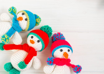 Three Little cute crocheted snowmans in a multicolor hats and scarfs on a white wooden background.