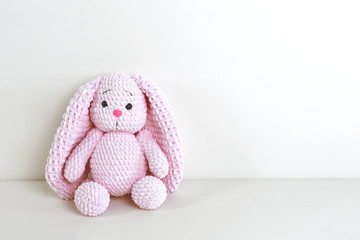 Fluffy pink bunny toy with long ears sitting near a white wall. Copy space.