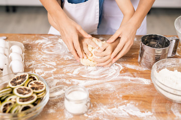 Female hands on those of little boy kneading dough for pastry on kitchen table