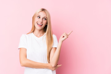 Young blonde woman on pink background smiling cheerfully pointing with forefinger away.