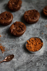 on a dark textured background with chocolate muffins and vintage spoon and cocoa powder.