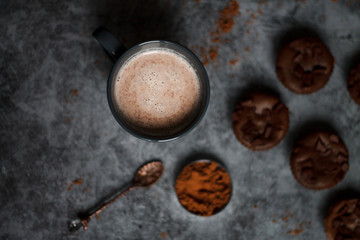 chocolate cocoa in blue mug on dark textured background with chocolate muffins and vintage spoon and cocoa powder.