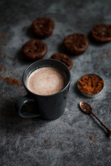 cocoa drink in blue mug with chocolate on dark textured background with chocolate muffins and vintage spoon and cocoa powder.