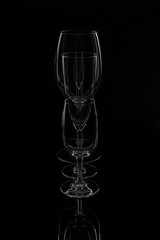 Empty clean wine glasses stand in a row one by one on a dark background with reflection.