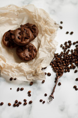 on a light textured marble background, chocolate muffins on parchment paper with a vintage spoon and coffee beans top view.