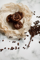 on a light textured marble background, chocolate muffins on parchment paper with a vintage spoon and coffee beans top view.