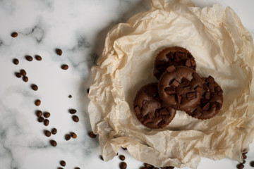on a light textured marble background, chocolate muffins on parchment paper with a vintage spoon and coffee beans top view.