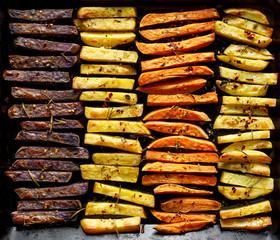 French fries,  baked fries from different types and colors of potatoes sprinkled with herbs and spices on a black background, top view