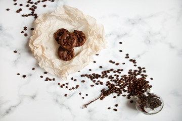 on a light textured marble background, chocolate muffins on parchment paper with a vintage spoon and coffee beans top view.