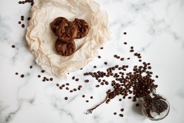 on a light textured marble background, chocolate muffins on parchment paper with a vintage spoon and coffee beans top view.