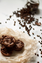 on a light textured marble background, chocolate muffins on parchment paper with a vintage spoon and coffee beans top view.