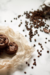 on a light textured marble background, chocolate muffins on parchment paper with a vintage spoon and coffee beans top view.