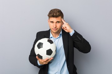 Young soccer trainer pointing his temple with finger, thinking, focused on a task.