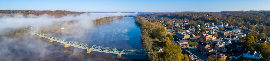 Large panoramic photo of river with bridge spanning to small river town during a fall sunrise