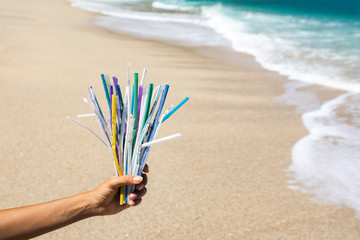 Fototapeta na wymiar Hand holding heap of used plastic straws on background of clean beach and ocean waves. Plastic ocean pollution, environmental crisis. Say no plastic. Single-use plastic waste