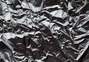 Crumpled silver aluminum foil closeup background texture. Abstract metallic paper holographic effect pattern
