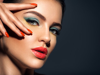 Beautiful woman with bright red lipstick on her lips. Gorgeous girl with blue eye makeup. Portrait of an attractive girl with orange nails on her face. Fashion  model. Sexy face of a pretty lady.