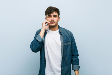 Young hispanic cool man with fingers on lips keeping a secret.