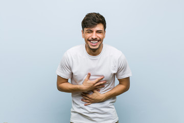 Young caucasian man wearing a white tshirt laughs happily and has fun keeping hands on stomach.