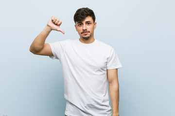 Young caucasian man wearing a white tshirt showing a dislike gesture, thumbs down. Disagreement...
