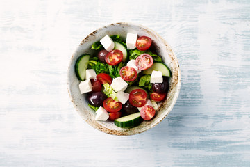 Salad with Kalamata Olives, Cucumber Cherry Tomatoes and Feta Cheese on bright wooden Background. Healthy Snack Idea. Top view. Copy space. 