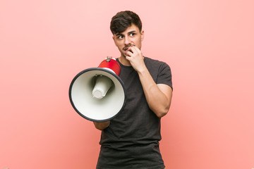 Young hispanic man holding a megaphone relaxed thinking about something looking at a copy space.