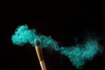Make-up brush with green powder explosion isolated on black background