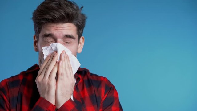 Young man sneezes into tissue. Isolated guy is sick, has a cold or allergic reaction. Health, medicine, illness, treatment concept