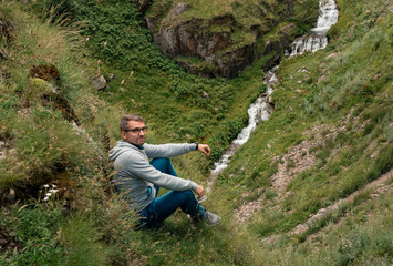 Naklejka na ściany i meble Man Traveler sitting on cliff with mountain river view. mountains success and fun euphoria emotions
