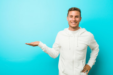 Young caucasian sport man showing a copy space on a palm and holding another hand on waist.