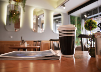 Close up paper cup of coffee and mafazine on table in the cafeteria.