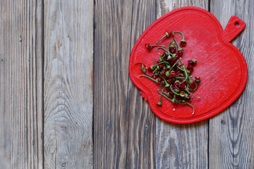 A large amount of dried pepper ponytails are in red, in the shape of an Apple, round plastic Board. Wooden background, top view, copy space, horizontal arrangement.