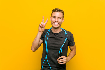 Young caucasian man holding a jump rope showing victory sign and smiling broadly.