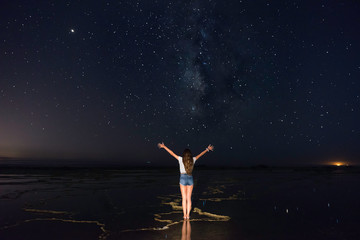 Fototapeta na wymiar Girl on a beach at night contemplating the Milky Way.