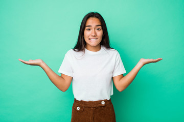 Young mixed race indian woman isolated confused and doubtful shrugging shoulders to hold a copy...
