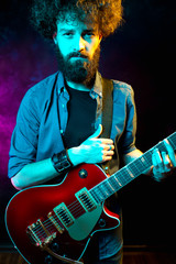 Close-up photo of hipster man with red guitar in neon lights. Rock musician is playing electrical guitar.