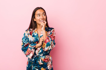 Young indian woman wearing a kimono pajama relaxed thinking about something looking at a copy space.