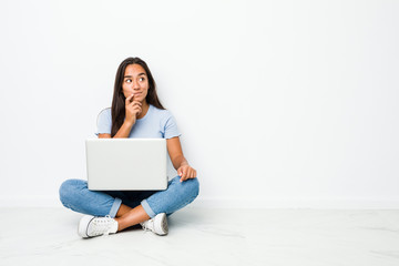 Young mixed race indian woman sitting working on laptop looking sideways with doubtful and skeptical expression.