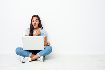 Young mixed race indian woman sitting working on laptop pointing to the side