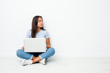 Young mixed race indian woman sitting working on laptop gazing left, sideways pose.