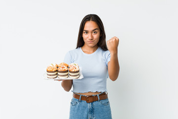 Young mixed race indian holding a sweet cakes showing fist to camera, aggressive facial expression.