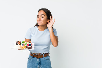 Young mixed race indian holding a sweet cakes trying to listening a gossip.