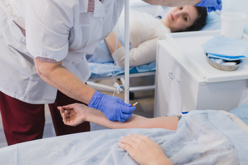 Nurse attaching intravenous tube to patient's hand in hospital bed