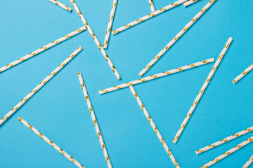 Festive white with gold drinking straws on a blue background. Holiday concept, decoration. Flat lay, top view