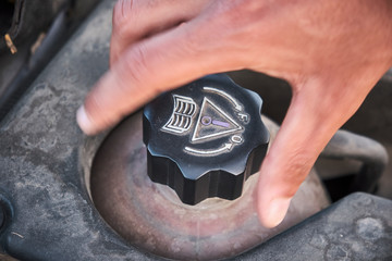 Brown man hands opening coolant liquid deposit container lid to check for a refill. Close-up.